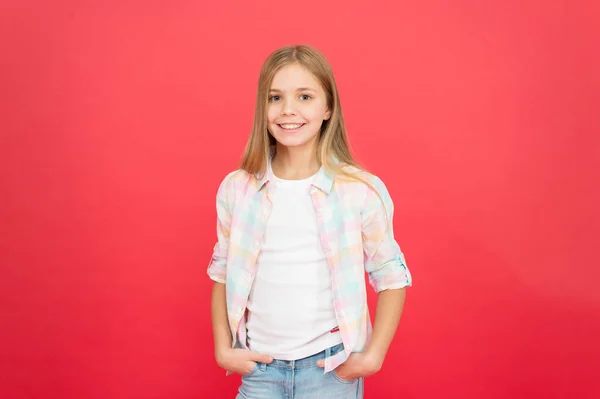 Op stijl. Kindermode. Stijlvolle schoonheid. klein meisje rode achtergrond. Gelukkige jeugd. glimlachend blond kind. meisje met lang blond haar. casual stijl. Dag van de kinderen. modieus klein meisje — Stockfoto