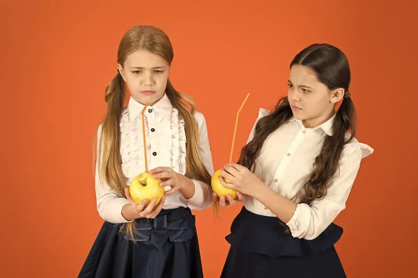 Impulsionar a aceitação estudantil de frutas. Distribuindo frutas frescas grátis na escola. Meninas crianças escola uniforme laranja fundo. As alunas comem maçãs. Almoço escolar. Nutrição vitamínica durante o dia escolar — Fotografia de Stock