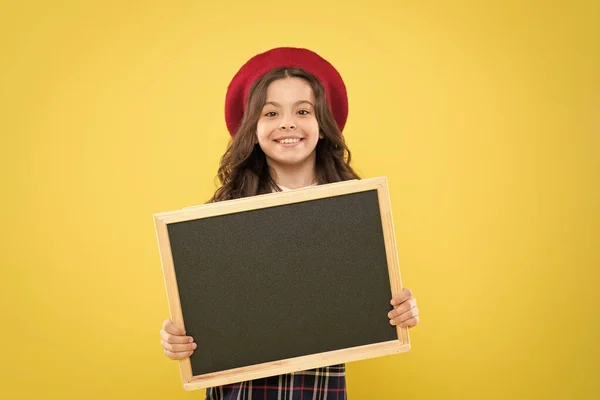 Klein meisje in Franse baret. Advertentie. kind met leeg Blackboard. Parijse kind op gele achtergrond. gelukkig meisje met krullend haar in baret. uw advertentie in goede handen. reclamebord — Stockfoto