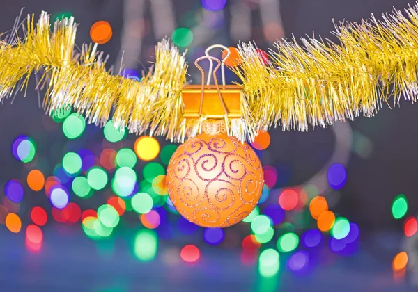 Christmas ornaments concept. Ball ornament hang on shimmering tinsel. Pick colorful decor for christmas tree. Tinsel with pinned christmas ornament on defocused garland lights background