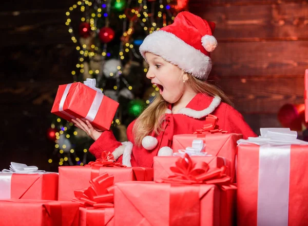 Санта приніс мені подарунки. Дитяча щаслива збуджена дівчина знаходить подарунки біля ялинки. Щаслива концепція дитинства. Дитячий одяг Санта-капелюх тримає загорнуту різдвяну подарункову коробку. Щастя і радість. Веселого Різдва — стокове фото