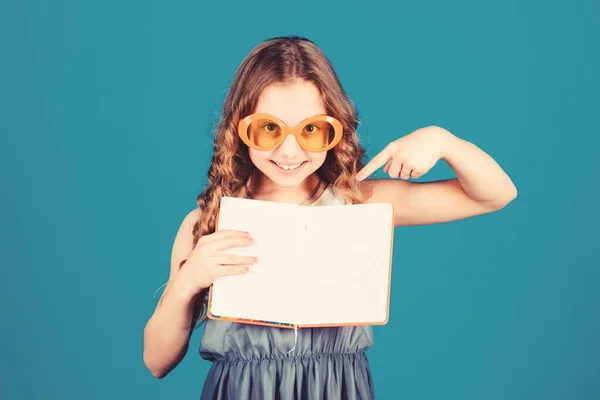 Kleine Schönheit Mädchen schreiben ihre Erinnerungen. Pläne für Sommerferien und Urlaub schmieden. Tagebuchnotizen. kleines glückliches Mädchen mit Brille und Notizbuch. Lesebuch. Sommermode. Kopierraum. Blick nach innen — Stockfoto