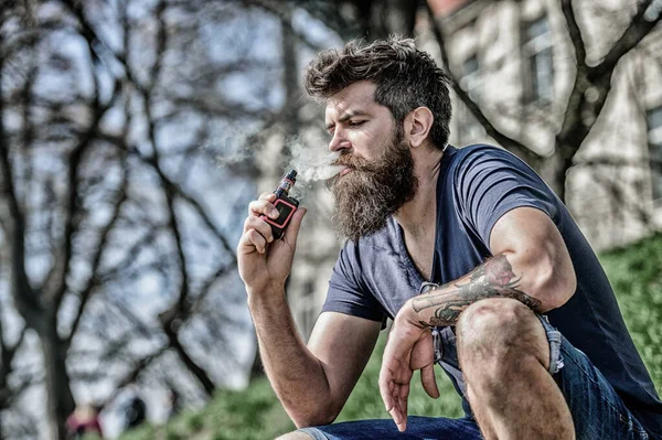 Dispositivo de fumar. Homem barba longa relaxado com hábito de fumar. Um homem com barba exala fumo. Nuvens de fumo aromatizado. Conceito de alívio de estresse. Homem barbudo a fumar vape. Fumar cigarro eletrônico — Fotografia de Stock