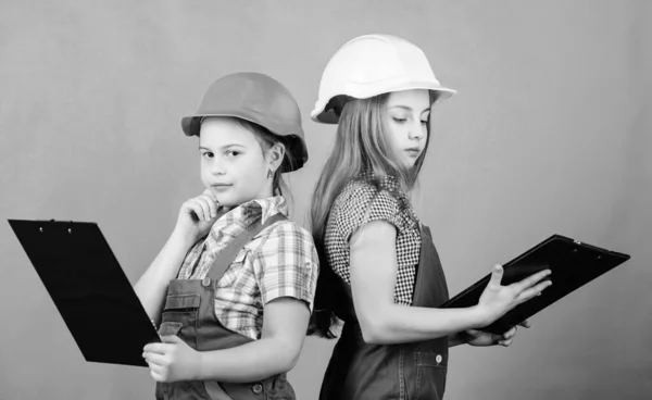 Trabajo en equipo.. Día del Trabajo. 1 de mayo. Niño pequeño con casco y tableta. Inspector Foreman. Reparar. niñas pequeñas que reparan juntos en el taller. Discutiendo algunos problemas. Tratando de encontrar lo que estaba roto —  Fotos de Stock