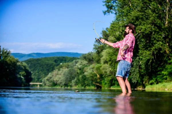 Amante della natura. pesca hipster con cucchiaio-esca. pescatore di successo in acqua di lago. hobby del pesce della mosca. Attività di pesca estiva. pesca d'altura. rilassarsi sulla natura. maturo uomo barbuto con pesce su asta — Foto Stock