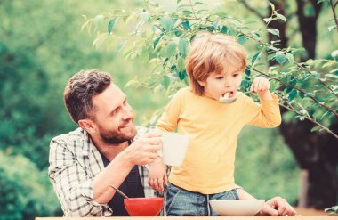 Baba oğul yemek yer ve eğlenir. Çocuklar için menü. Aile ev yapımı yemeklerin tadını çıkarır. Yemek alışkanlıkları. Baba ile küçük çocuk yemek piknik bahçesinde doğa arka plan yiyor. Yaz kahvaltısı. Sağlıklı gıda kavramı