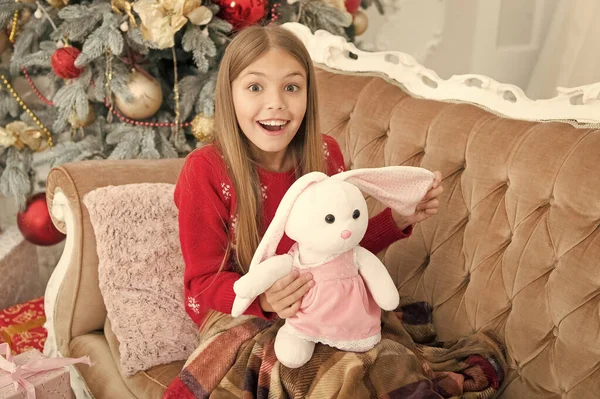 Isto é inacreditável. Menina com coelhinho bonito na árvore de Natal. Criança pequena feliz sorrindo com presente. Menina pequena segurar brinquedo de coelho. Pequena criança brincar com brinquedo macio. Melhor brinquedo de Natal — Fotografia de Stock