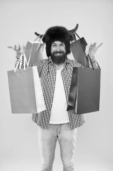 Sigue sonriendo y lleva las maletas. Hombre barbudo sonriendo con bolsas de papel después de la venta estacional. Feliz hipster con cuernos de toro sombrero sosteniendo bolsas de compras. Llevar compras en coloridas bolsas de transporte no de comestibles — Foto de Stock