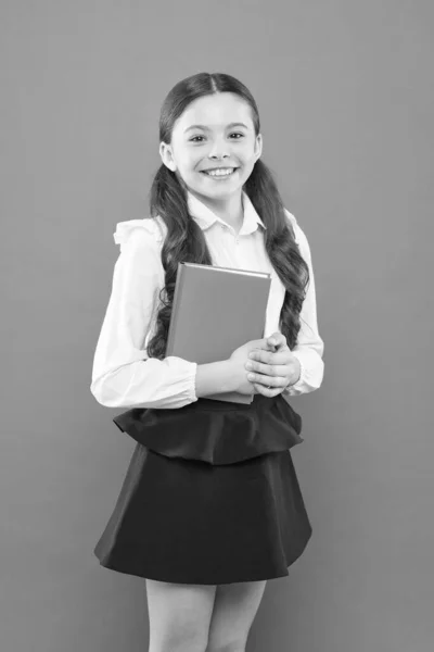 Schoolgirl skriva anteckningar på Orange bakgrund. liten flicka i skoluniform. läs lektion. informationsblankett bok. tillbaka till skolan. Happy Child koncentrerade sig på arbetet. Lektion i skolan. Smart Skolflicka — Stockfoto