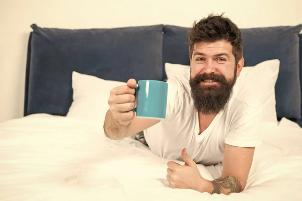 Full of energy. Coffee affects body. Man handsome hipster relaxing on bed with coffee cup. Bearded hipster enjoy morning coffee. Morning becomes much better with good coffee. Relax and rest