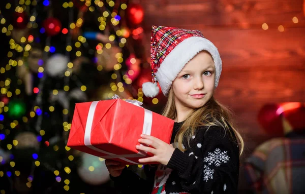 Holiday party that actually sounds fun. Merry christmas. Kid adorable wear santa hat celebrate christmas. Winter shopping. Buy christmas gift. Girl cute child hold wrapped gift near christmas tree — Stock Photo, Image