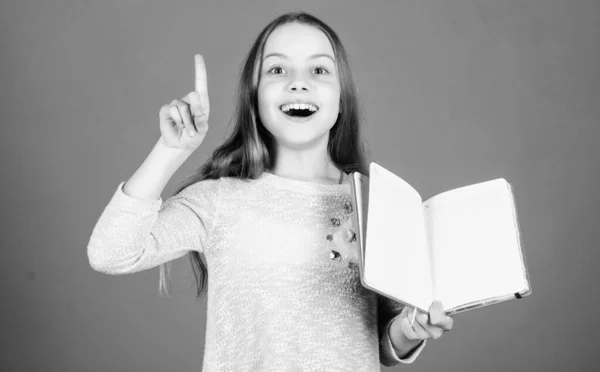 J'ai une super idée. Bonne petite fille tenant le livre d'idées ouvert et gardant le doigt levé. Souriant petit enfant ayant une idée. L'idée lui est venue à l'esprit, copier l'espace — Photo