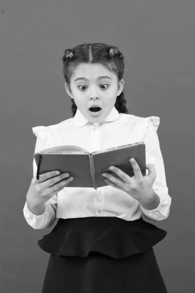 What a surprise news. Surprised girl reading book on red background. Adorable little child with surprise emotion on face. Cute small girl keeping mouth opened of big surprise. Surprise concept — Stock Photo, Image