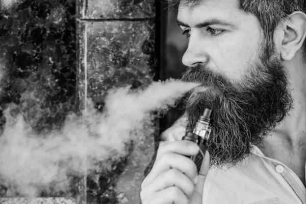 Человек с бородой выдыхает дым. Курение электронных сигарет. Концепция снятия стресса. Курящее устройство. Мужчина с длинной бородой, расслабленный от курения. Облака ароматизированного дыма. Бородатый человек курит vape — стоковое фото