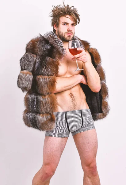 Moda y pathos. Riqueza y concepto de lujo. Chico atractivo rico posando abrigo de piel en cuerpo desnudo. Atleta rico disfrutar de su vida. Sexy soñoliento rico macho tousled pelo beber vino aislado en blanco — Foto de Stock