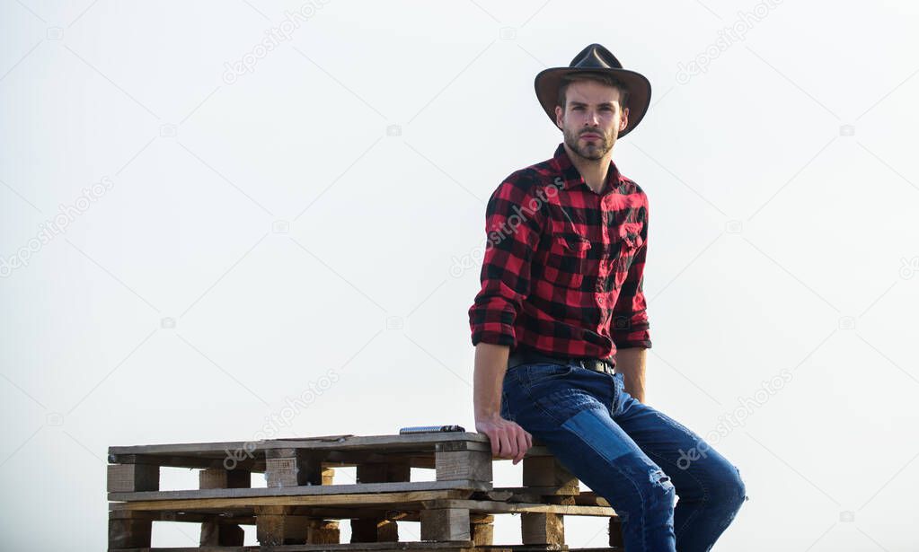 from the country. Vintage style man. Wild West retro cowboy. cowboy sit on woden pallet. Western. man checkered shirt on ranch. western cowboy portrait. wild west rodeo. Thoughtful man in hat relax