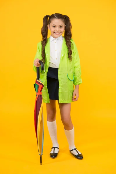 Niedlich und praktisch. glückliches kleines Mädchen mit Regenschirm und elegantem Stil auf gelbem Hintergrund. Ein kleines Kind lächelt im Regenbogenkostüm. Mode für die Regenzeit — Stockfoto