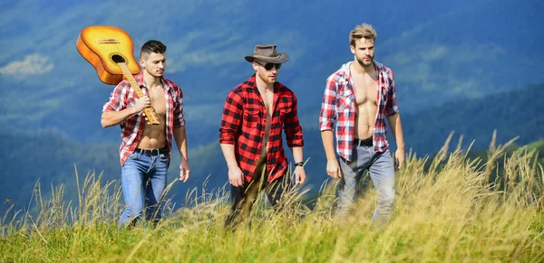 Tourists hiking concept. Hiking with friends. Enjoying freedom together. Long route. Group of young people in checkered shirts walking together on top of mountain. Men with guitar hiking on sunny day