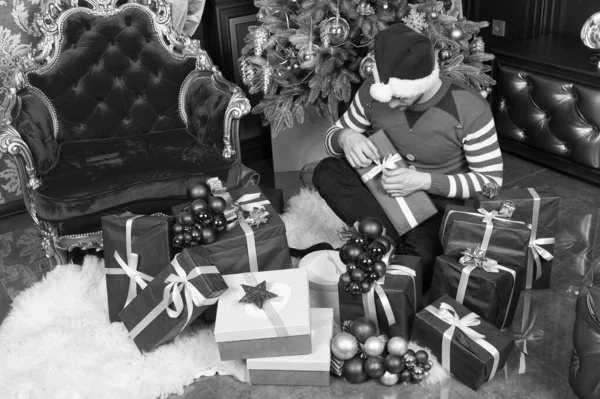 Genieten van de kerst. Man in KERSTMUTS houden Kerstcadeaus. Guy viert kerst thuis. Levering Kerstcadeaus. Gelukkig man met kerst geschenkdozen. Krijgen in de geest van het seizoen — Stockfoto