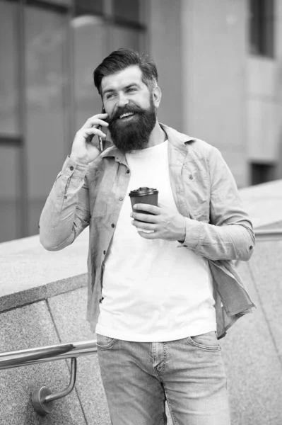 Mantenha-se em contacto. Homem barbudo andar com smartphone e copo de café fundo urbano. Homem sorridente rosto smartphone. Guy satisfeita chamada resposta smartphone. Conceito de comunicação. Fico feliz em ouvir. Boas notícias. — Fotografia de Stock