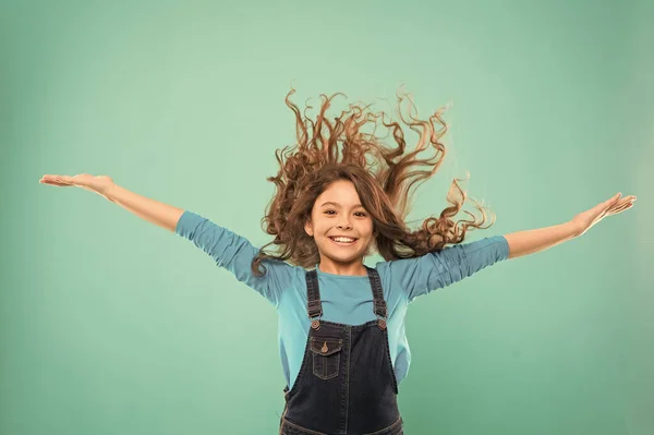 Experiencing a hair to balance your energy. Adorable girl curly hair waving on blue background. Small cute girl with long brunette hair wearing casual style. Little hair model with fashion look — Stock Photo, Image