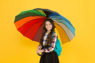 Yağmurlu hava ve uygun giysiler. - Okula gidiyorum. Neşeli gülümseyen liseli kız. Yağmurlu gün eğlencesi. Şemsiye altında iyi yürüyüşler. Yağmur konseptinin tadını çıkar Çocuk mutlu renkli gökkuşağı şemsiyesi tutun