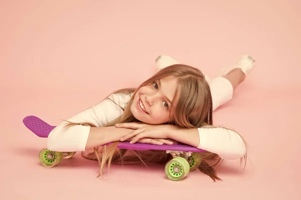 Поширюючи щасливі вібрації з дошкою пенні. Маленька дівчинка ковзанярка розслабляється на дошці копійки на рожевому фоні. Маленька дитина посміхається з фіолетовою дошкою пенні. Щасливий хіпстер з копійки скейтборд — стокове фото