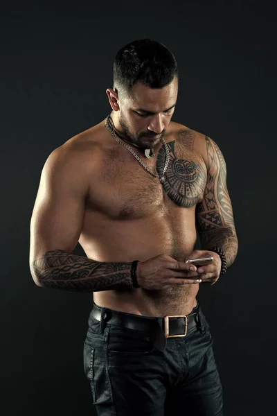 メッセージを送信します。ハンサムなフィット男は送信メッセージのスマート フォンです。魅力的な筋肉入れ墨選手の表情。メッセージング通信の概念。男ハンサムな上半身裸暗い背景上のジーンズと筋肉 — ストック写真