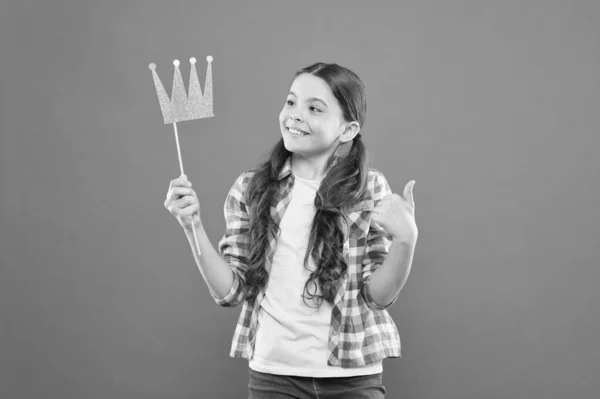 Ese orgullo suyo. Linda niña pequeña sosteniendo la corona de utilería con orgullo sobre fondo naranja. Adorable princesita sintiendo gran orgullo de corona en palo. Orgullo y alegría — Foto de Stock