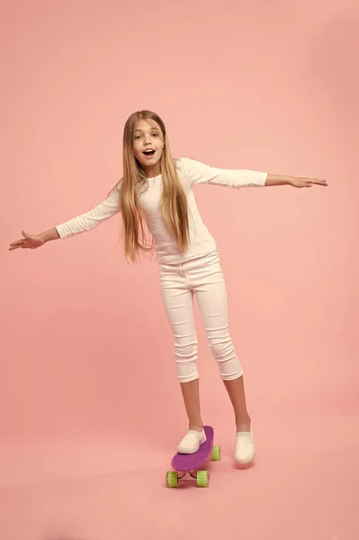 Opnieuw genereren van haar energie skateboarden. Schattig klein kind het uitvoeren van skateboarden trucs op roze achtergrond. Schattig klein meisje skateboarden op Violet Penny Board. Ga skateboarden dag — Stockfoto