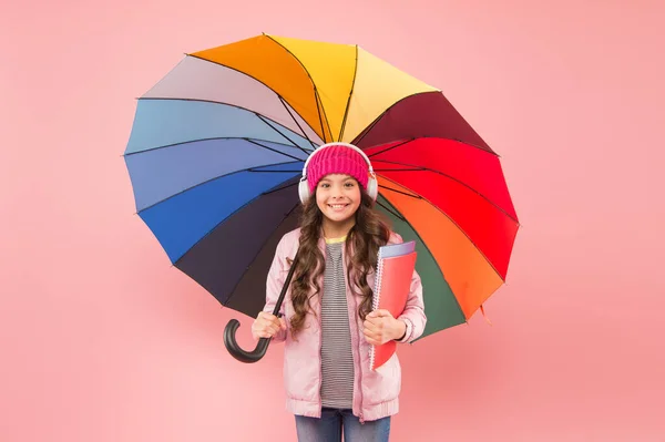 Navrženo pro deštivé počasí. Malá školačka drží barevný deštník na růžovém pozadí. Malé dítě zpět do školy na podzim. Roztomilé dítě ve sluchátkách chodí v deštivý den do školy. Nejlepší škola — Stock fotografie