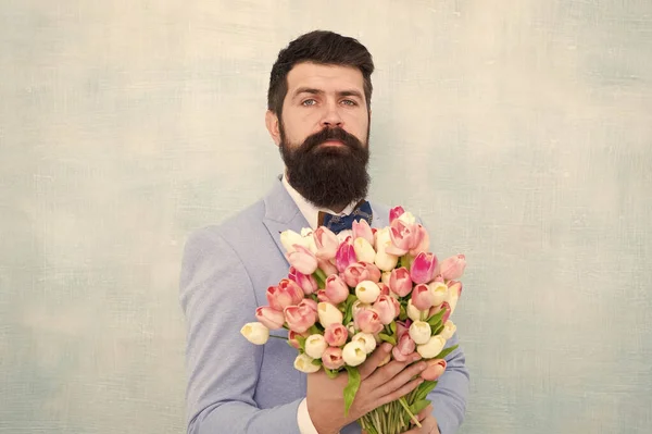 Flowers for her. Man bearded suit bow tie hold tulips bouquet. Gentleman making romantic surprise for her. Flowers delivery. Gentleman romantic date. Birthday greetings. Best flowers for girlfriend