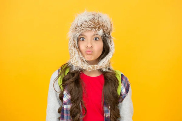 Sending air kiss. Small kid with kiss lips on yellow background. Little kid wear fur hat in casual winter style. Cute fashion kid. Small kid with beauty look