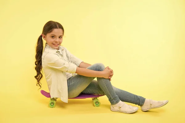 女の子に乗るペニーボード黄色の背景。ペニーボードで楽しんでいる子供。趣味好きな活動。子供の笑顔スケートボードに座っている。ペニーボード女の子のためのかわいいカラフルなスケートボード。乗ろう — ストック写真
