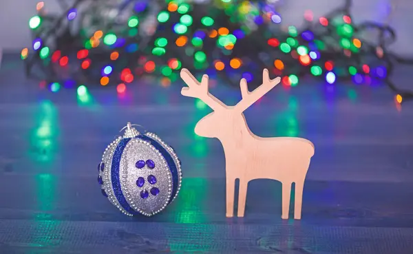 Bola con adornos y juguete de ciervo de madera sobre fondo de guirnalda colorido borroso. Decoración de Navidad. Símbolos de las vacaciones de invierno de Navidad. Ciervo y adorno decorativo de juguete. Feliz concepto de Navidad —  Fotos de Stock