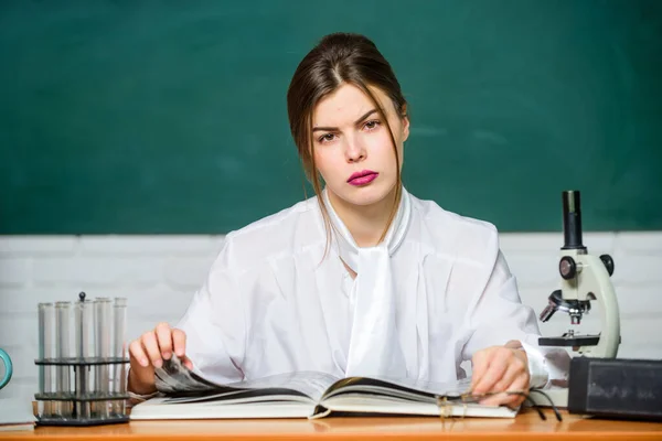 Student biologii siedzi w klasie w tle tablicy. Mądra studentka. Ucz się. Badania naukowe. Koncepcja edukacji. Kobieta jest uroczą nauczycielką lub uczennicą. Biolog chemik z mikroskopem — Zdjęcie stockowe