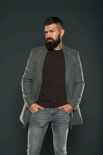 A barba fica na moda. Homem da moda. Modelo de moda mantendo os braços nos bolsos em fundo cinza. Homem barbudo com aparência de moda. Brutal hipster com barba e bigode cabelo em estilo casual — Fotografia de Stock