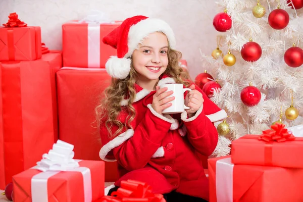 Ulubiony napój kakaowy. Kapelusz Mikołaja lubi napój kakaowy. Idealny sposób, aby ogrzać Ci sezon wakacyjny. Dziewczyna małe słodkie dziecko trzymać kubek z gorącym napojem podczas świętowania Bożego Narodzenia. Gorące kakao w Wigilię — Zdjęcie stockowe