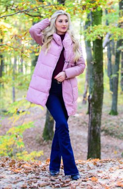 Sonbahar ormanlarında şık sarışın kız yürüyüşü. Herkesin giymesi gereken ceketler. Almak için en iyi kabarık ceketler. Bir yıldız gibi rockçı ceketi nasıl giyilir? Puffer moda konsepti. Kadın kalın pembe ceket giyiyor.