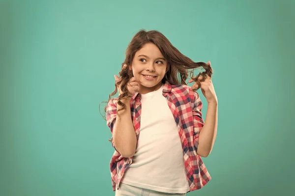 Riccioli giocosi. Consigli di bellezza per capelli ordinati. Ragazza lunga capelli lucidi sani portare vestiti casual. Ragazzina con i capelli lunghi. Ragazzo felice viso carino con adorabili capelli ricci stand su sfondo blu — Foto Stock