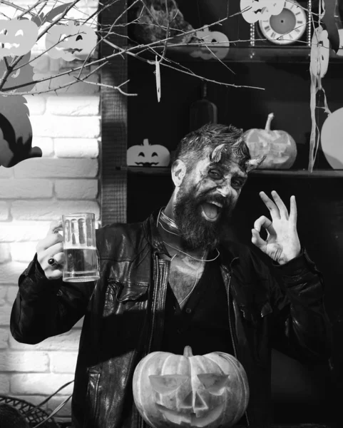 Man wearing scary makeup holds mug of beer on Halloween
