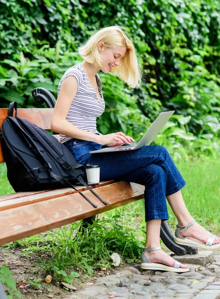 Modern diákélet. Rendes diák. Szörfözök az interneten. Lány imádnivaló diák laptoppal és kávéscsészével ül padon a parkban. Női tanulók jegyzetfüzetekkel dolgoznak. Tanulmányi felfedezés. Kültéri tanulmányok — Stock Fotó