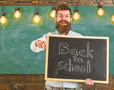 Gözlüklü öğretmen karatahtaya yazı yazmış. Okul konseptine geri dönelim. Mutlu yüzlü sakallı ve bıyıklı adam öğrencileri davet ediyor, ileri bakan, arka grubunda yazı tahtası olan