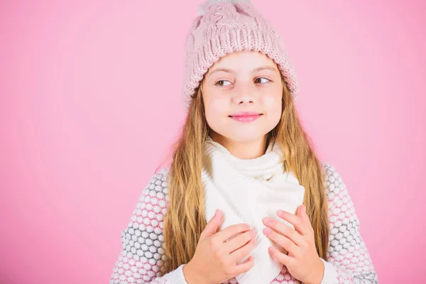 Varmt tilbehør som vil gjøre vinteren koselig. Lang, barnelangt hår, varm og myk hatt. En liten jente med strikket, varm hatt, avslappende rosa bakgrunn. Vinterkleskonseptet – stockfoto