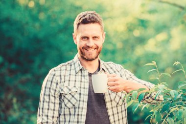 Ferahlatıcı bir içki. Adam sakallı çay çiftçi kupa doğa arka plan tutun. Yeşil çay tarlası. Bütün yaprak çayı. Mükemmel bir tat. Sıcak içeceklerin tadını çıkarın. Doğal içecek. Sağlıklı yaşam tarzı. Yeşil çayı tercih ederim.