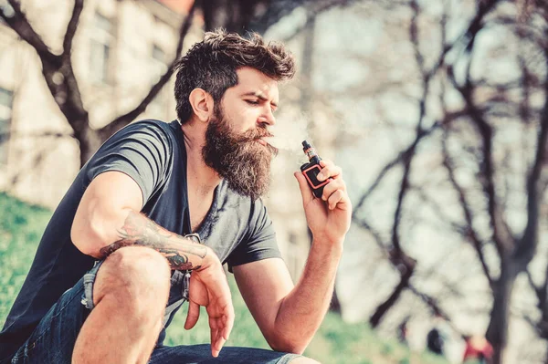 Smoking device. Man long beard relaxed with smoking habit. Man with beard breathe out smoke. Clouds of flavored smoke. Stress relief concept. Bearded man smoking vape. Smoking electronic cigarette