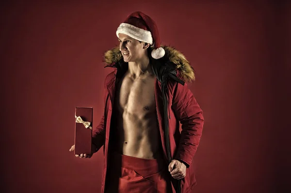 Dárkové zásilková služba. Pohledný santa koncept. Muž sportovec nosit klobouk santa. Macho svalnatý trup pózuje s dárkovou krabičku. Santa claus dárky courier. Sexy sportovní macho svalnatou hruď v santa claus klobouk — Stock fotografie