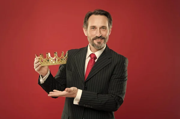 Rik belöning. Mogen affärsman som visar krona belöning på röd bakgrund. Successfil Big Boss belönar vinnaren med värdefull belöning för framgång. Vinnande värdefullt pris och belöning — Stockfoto
