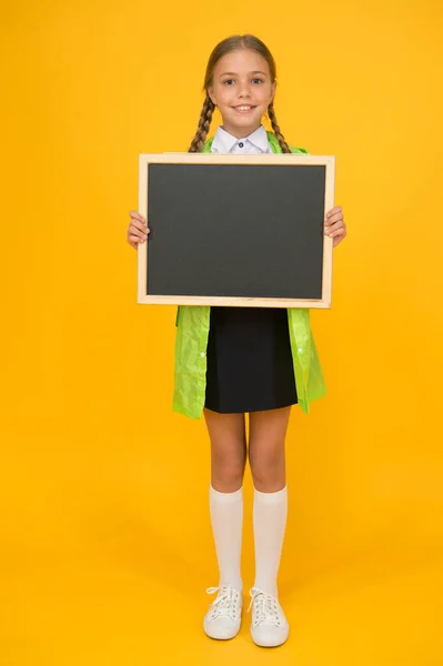 気をつけてね幸せな女の子は黄色の背景に学校の黒板を保持します。空白の黒板を持つ小さな子供。小さな子供が授業のために黒板を手に入れた。学校広告のBlackboard 、スペースのコピー — ストック写真
