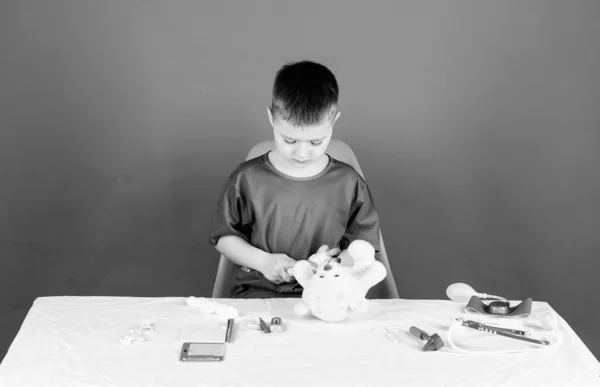 Niño lindo niño futuro médico carrera. Trabajador del hospital. Salud. El pequeño doctor está ocupado sentándose en la mesa con herramientas médicas. Examen médico. Concepto de medicina. Procedimientos médicos para oso de peluche — Foto de Stock